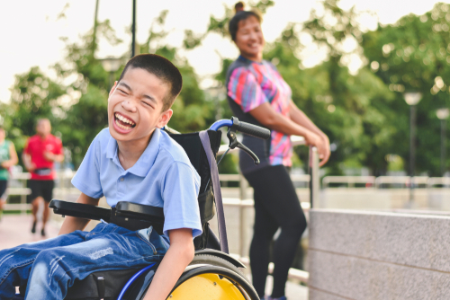 a mother and son at a park. The son is using a wheelchair rental