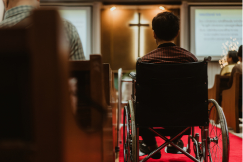 Man in wheelchair sits in the aisleway of a church during a service