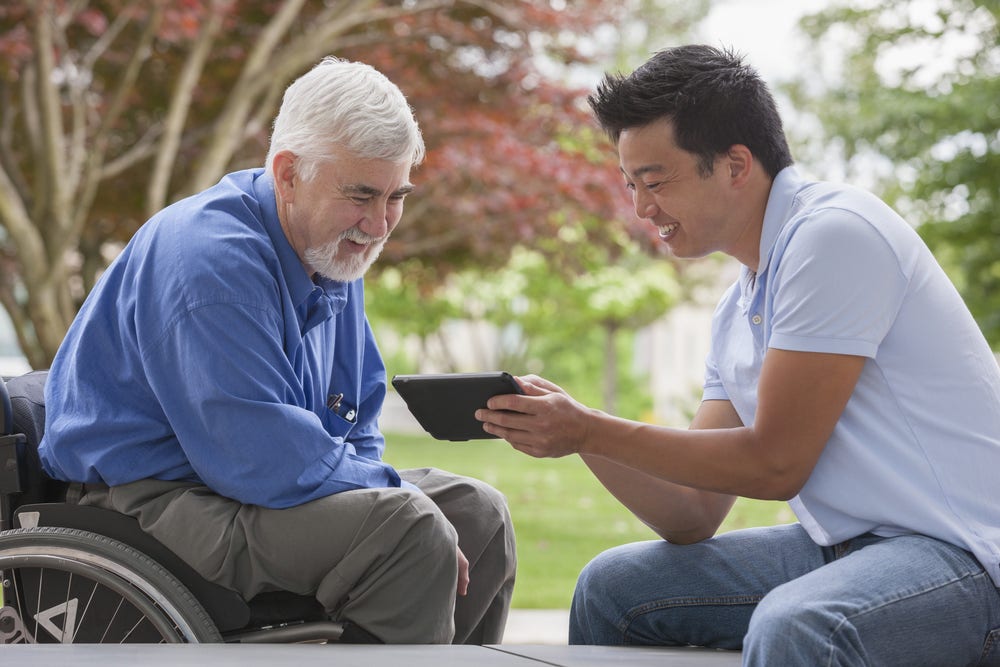 Engineer with muscular dystrophy and diabetes in his wheelchair talking with design engineer using tablet Engineer with muscular dystrophy and diabetes in his wheelchair talking with design engineer using tablet