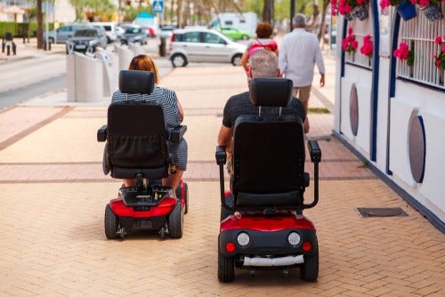 Couple elderly people ride along the sidewalk to an electric wheelchair. Motorized wheelchair. Mobile scooter. Couple elderly people ride along the sidewalk to an electric wheelchair. Motorized wheelchair. Mobile scooter.