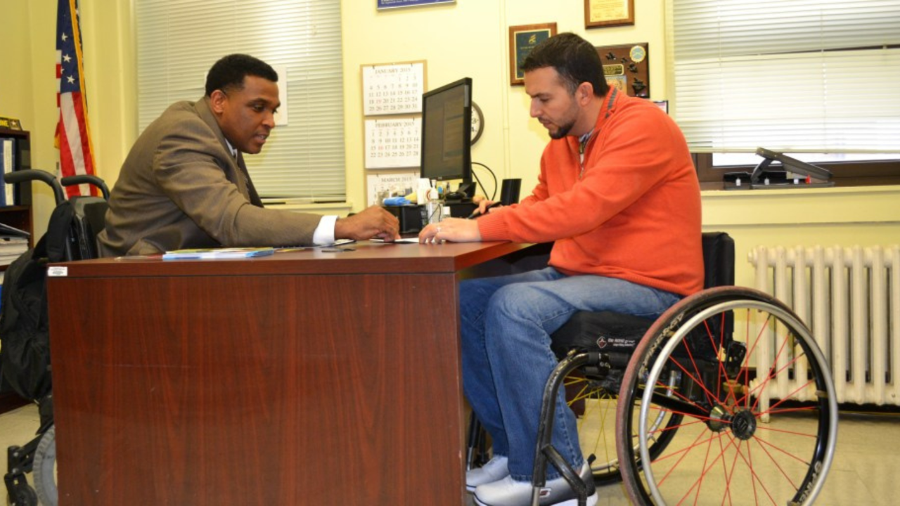 Man in wheelchair signing papers at a desk