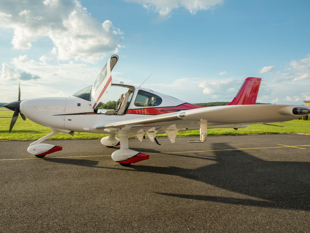 A white and red prop plane stands open on a runway on a sunny day