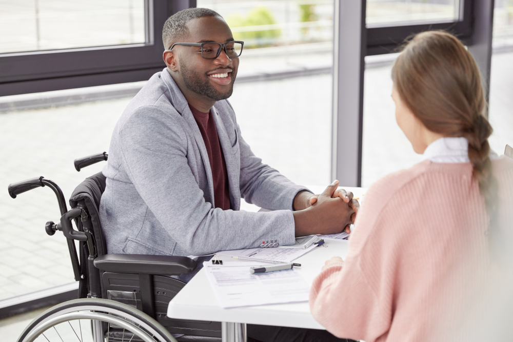 Handsome cheerful black male in wheelchair involved in charity, meets with female investor, discuss main details, helps physically challenged people. People, health and business concept