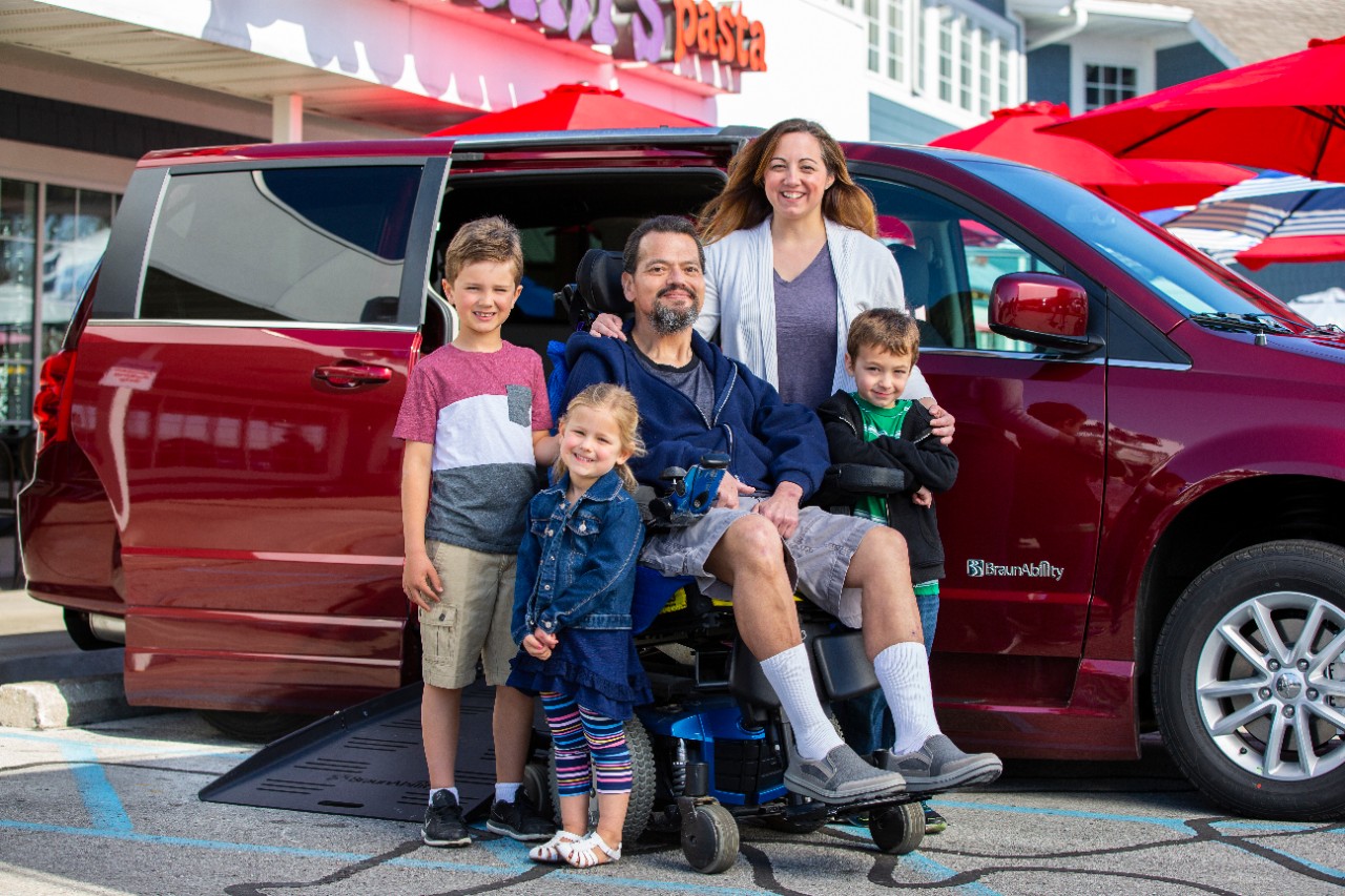 wheelchair user and his family sitting outside of a business next to a red dodge wheelchair van