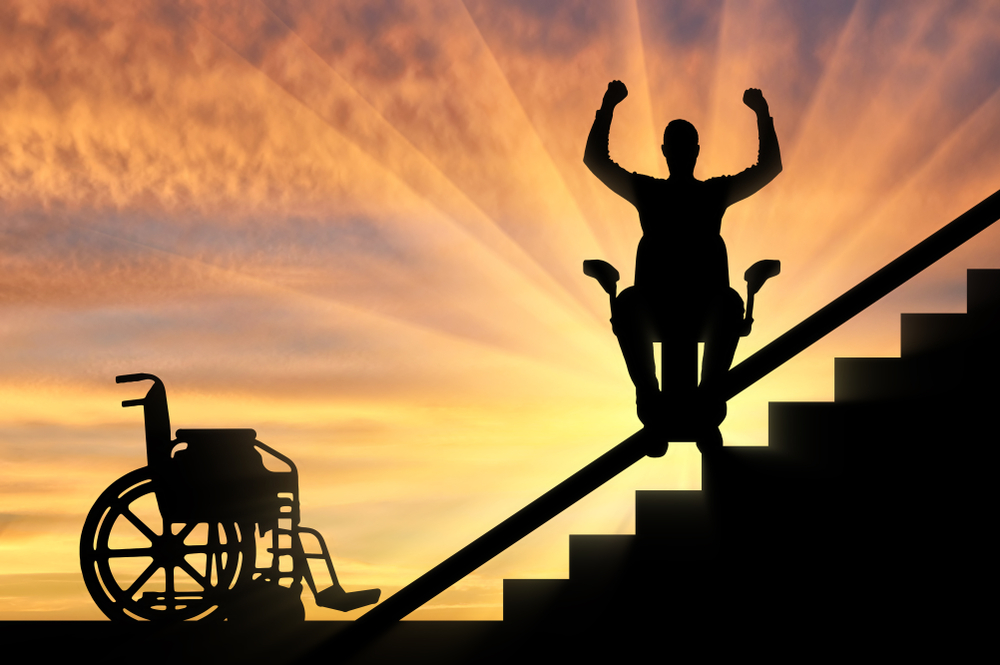 Wheelchair sits at bottom of staircase. Person uses stair lift to climb stairs