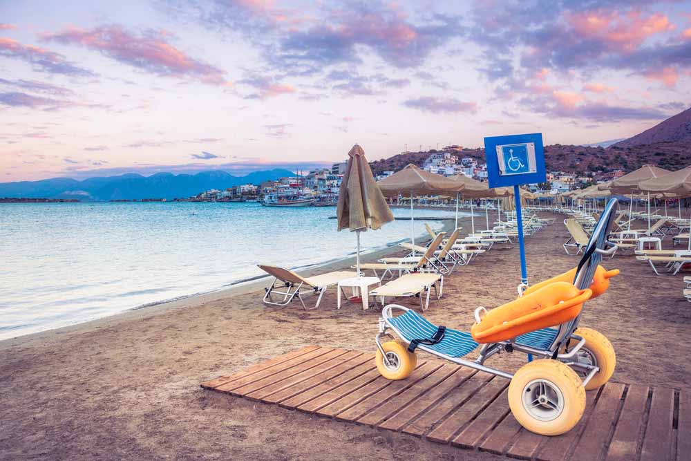 A beach wheelchair sitting on a beach next to many umbrellas 