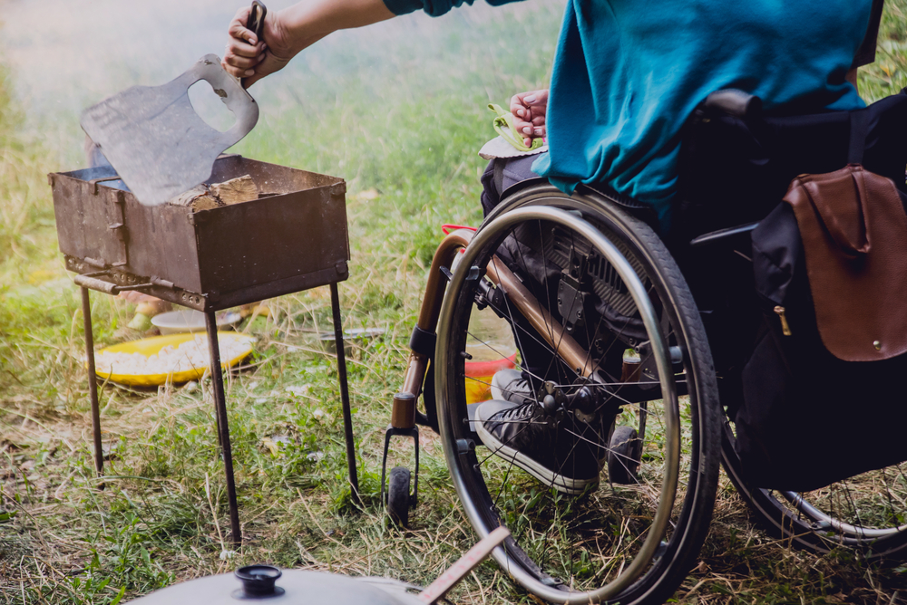 person in a wheelchair grilling food while camping