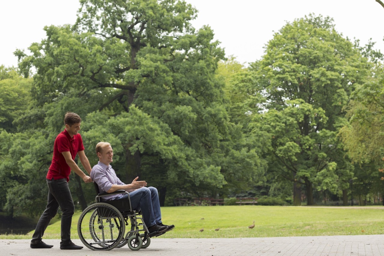 Shot of a young man and his friend in a wheelchair having a walk in a park