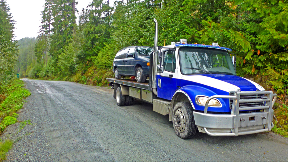 A flatbed tow truck towing a minivan
