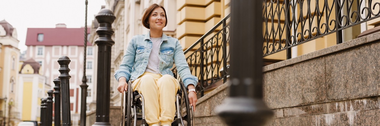 Brunette woman smiling and sitting in wheelchair on city street