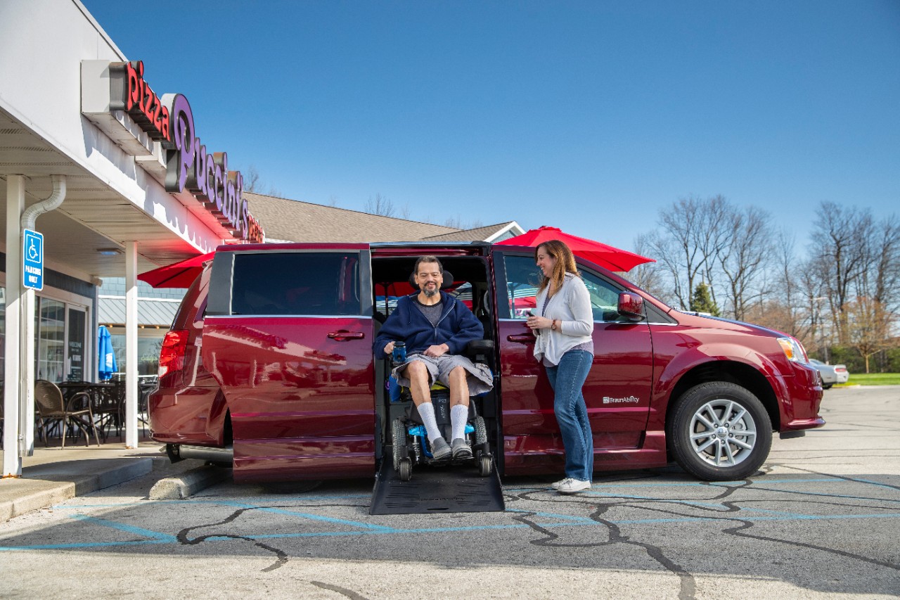 Man exits a BraunAbility side-entry Dodge van in a power chair while his wife stands to the side Man exits a BraunAbility side-entry Dodge van in a power chair while his wife stands to the side