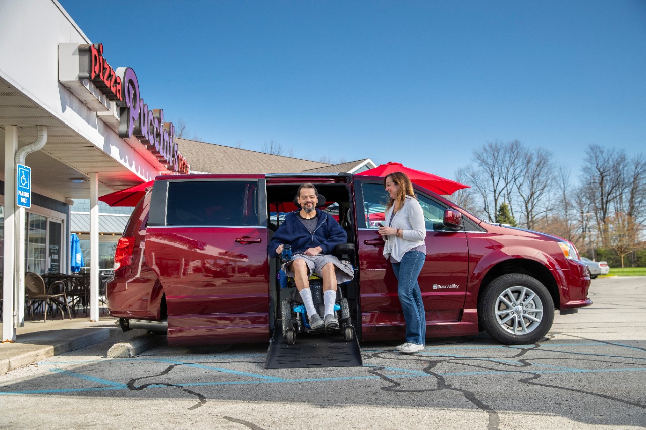 Man exits a BraunAbility side-entry Dodge van in a power chair while his wife stands to the side