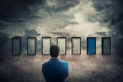 Rear view of a businessman in front of many doors choosing the one different colored. Difficult decision, concept of the important choice in life, failure or success. The ways to unknown future, busin Rear view of a businessman in front of many doors choosing the one different colored. Difficult decision, concept of the important choice in life, failure or success. The ways to unknown future, busin