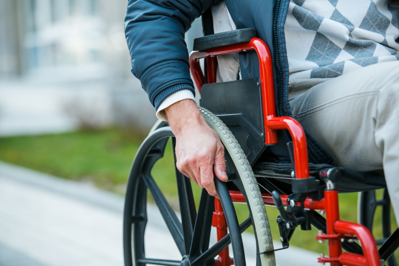 Adult man in wheelchair. Close up photo of male hand on wheel of wheelchair during walk