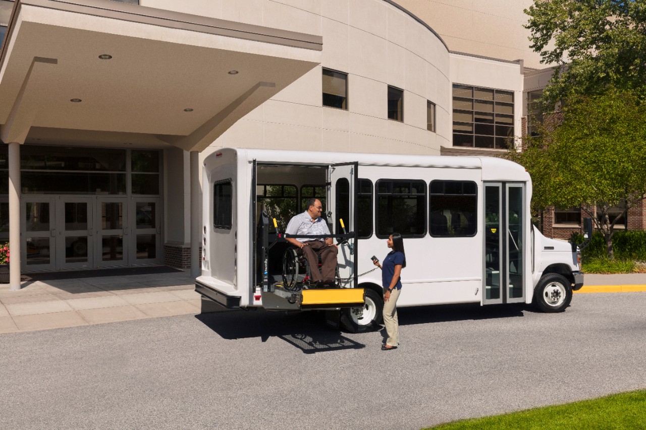 century wheelchair lift installed on a bus with a man in a wheelchair and a lady operating the wheelchair lift