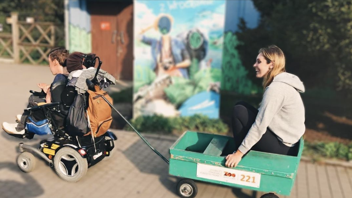 Shane Burcaw and Hannah Aylward traveling together. Shane is pulling Hannah in a wagon.