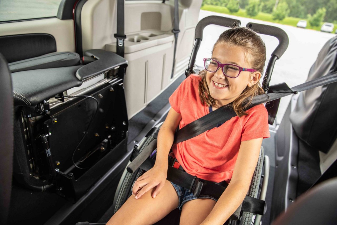 A young girl smiles while secured in a wheelchair in a rear-entry accessible vehicle A young girl smiles while secured in a wheelchair in a rear-entry accessible vehicle