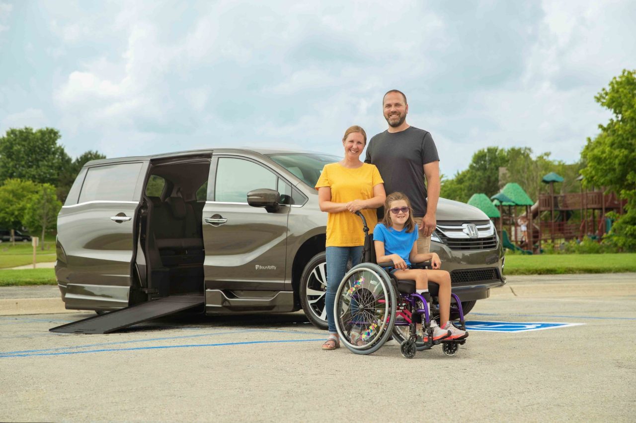 Young family with daughter in a wheelchair smiles in front of a Honda SE