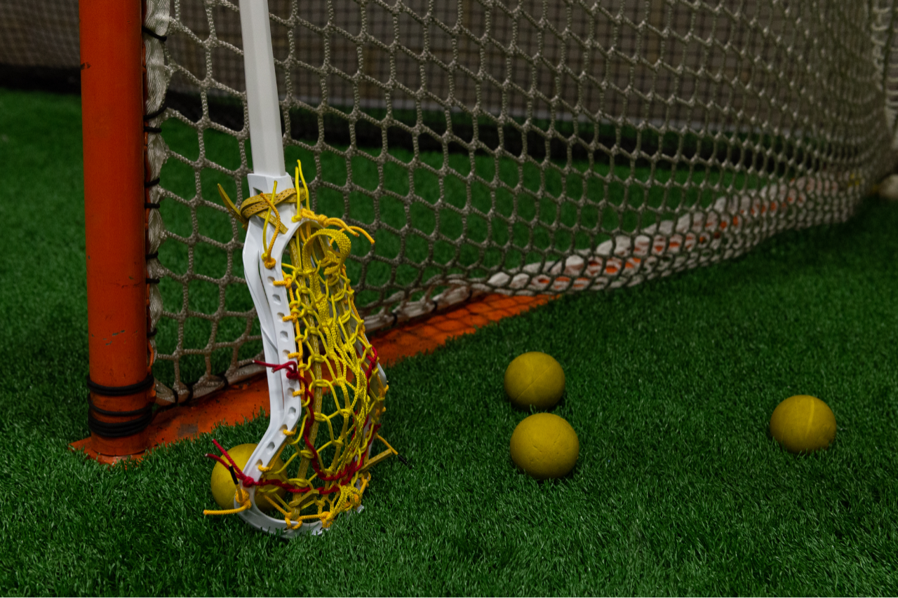 Woman's lacrosse stick leaning against a goal post with lacrosse balls nearby 