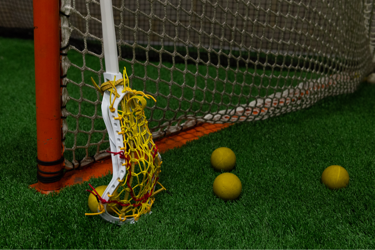Woman's lacrosse stick leaning against a goal post with lacrosse balls nearby Woman's lacrosse stick leaning against a goal post with lacrosse balls nearby