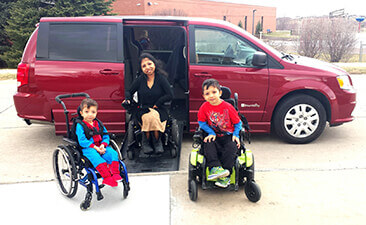 Mother and two sons all in wheelchairs smile from outside of their red BraunAbility van Mother and two sons all in wheelchairs smile from outside of their red BraunAbility van