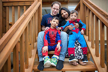 Dad, mom, and two sons dressed like super heroes pose for a photo on a staircase Dad, mom, and two sons dressed like super heroes pose for a photo on a staircase